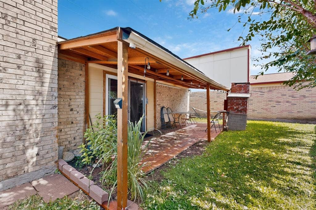2228 Bunker Hill Drive, Carrollton, TX 75006 Covered patio featuring wood-frame construction, brick exterior walls, masonry flooring, and a built-in outdoor masonry fireplace