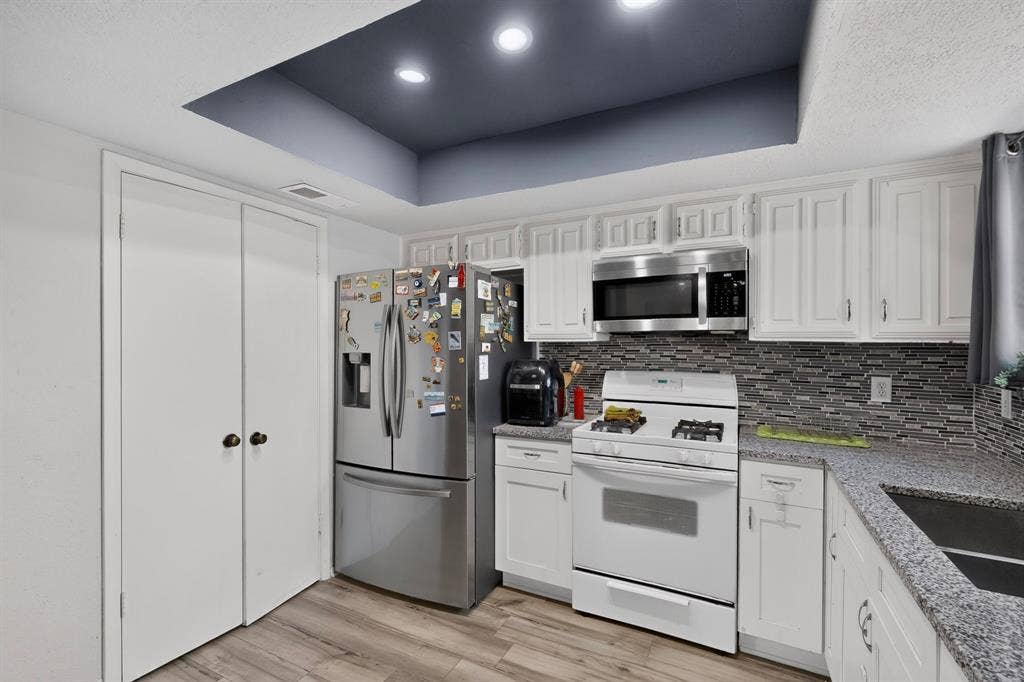 2228 Bunker Hill Drive, Carrollton, TX 75006 Kitchen featuring white shaker-style cabinetry, stone-finish countertops, decorative mosaic tile backsplash, recessed ceiling lighting, and wood-finish flooring