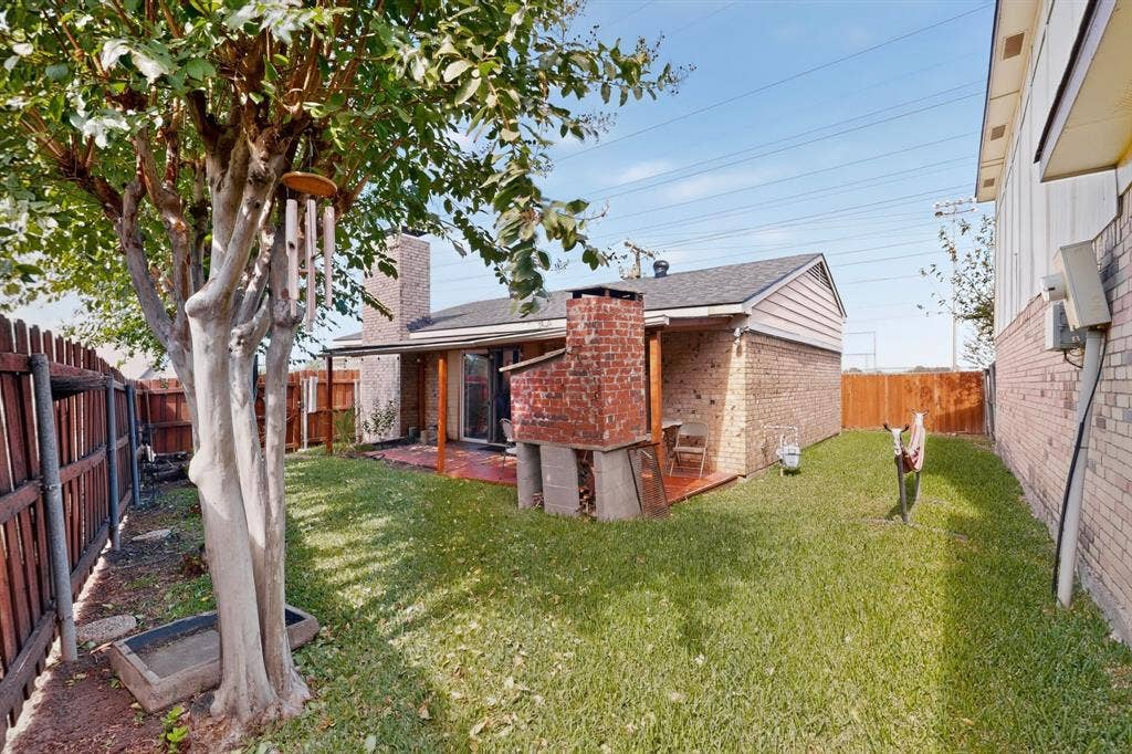 2228 Bunker Hill Drive, Carrollton, TX 75006 Rear exterior featuring a brick fireplace, covered patio, wood fencing, and mature landscaping