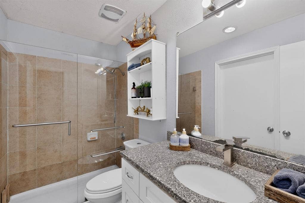 2228 Bunker Hill Drive, Carrollton, TX 75006 Bathroom featuring a vanity with a stone-composite countertop, integrated oval basin, and metallic fixtures, complemented by a tiled shower enclosure with a glass panel and mounted support rails