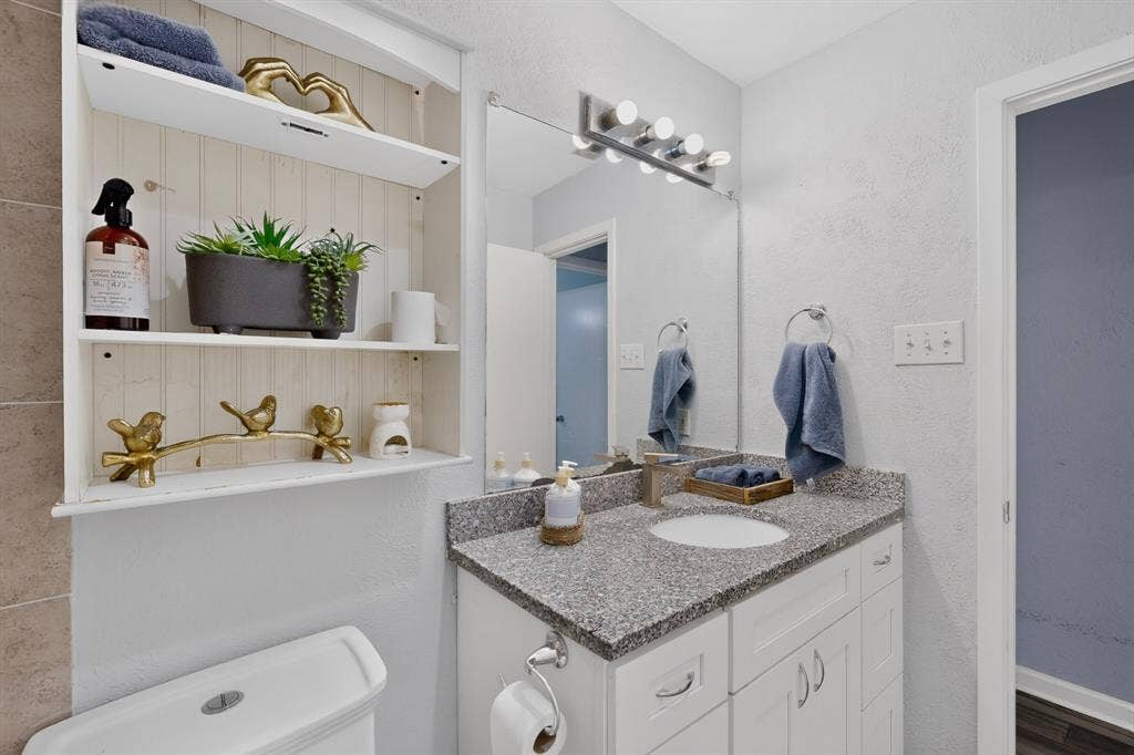 2228 Bunker Hill Drive, Carrollton, TX 75006 Built-in recessed shelving with beadboard backing, white vanity cabinet with stone-finish countertop, undermount sink, and four-light wall-mounted vanity fixture