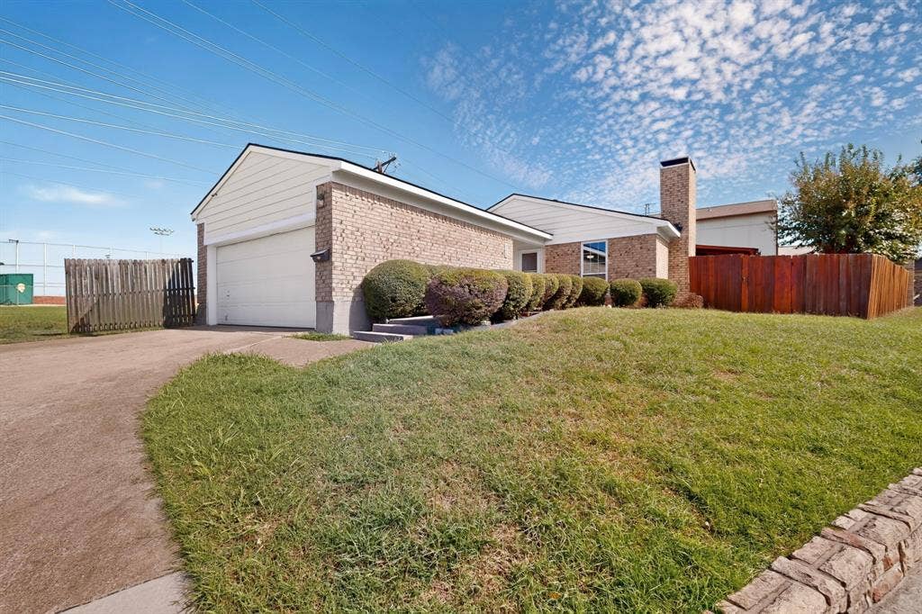 2228 Bunker Hill Drive, Carrollton, TX 75006 Exterior featuring a brick and horizontal siding facade, a two-car garage, an attached masonry chimney, and wood perimeter fencing