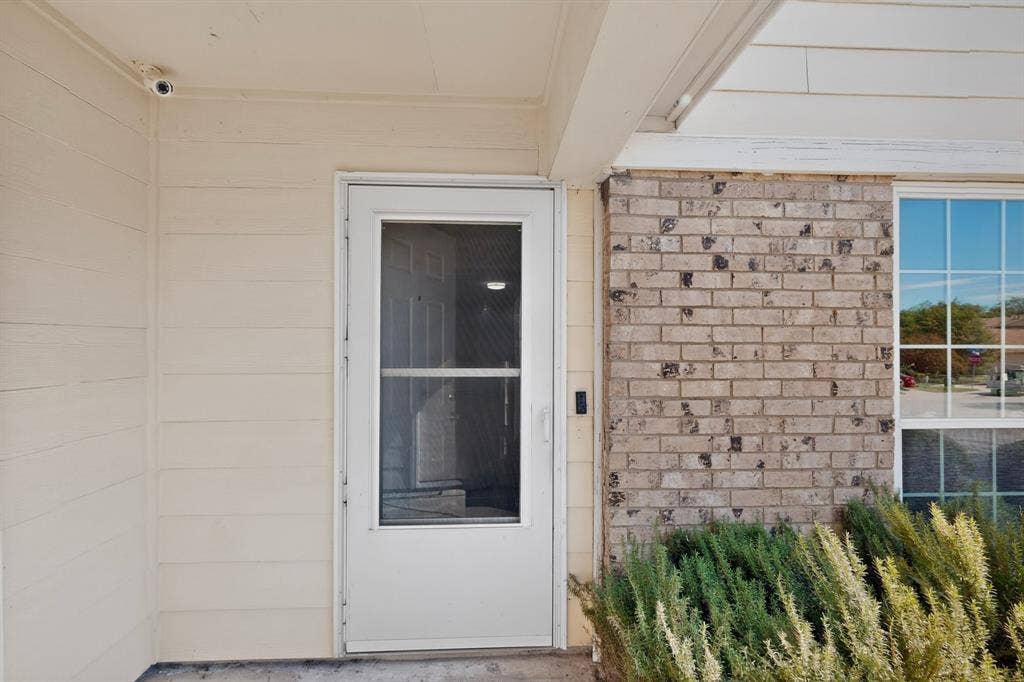 2228 Bunker Hill Drive, Carrollton, TX 75006 Entryway featuring a white storm door, beige horizontal lap siding, tan brick masonry, and a multi-pane window