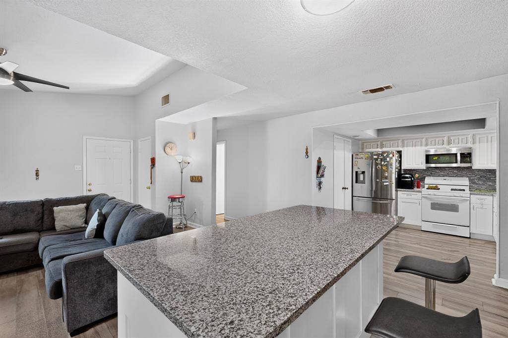 2228 Bunker Hill Drive, Carrollton, TX 75006 Kitchen featuring a stone-topped island, white cabinetry, integrated stainless steel appliances, and wood-finish flooring