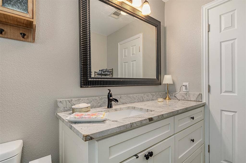 519 MAE Drive, Mabank, TX 75147 Vanity featuring a stone countertop with an integrated basin, matte black faucet, white shaker-style cabinetry, and a framed mirror