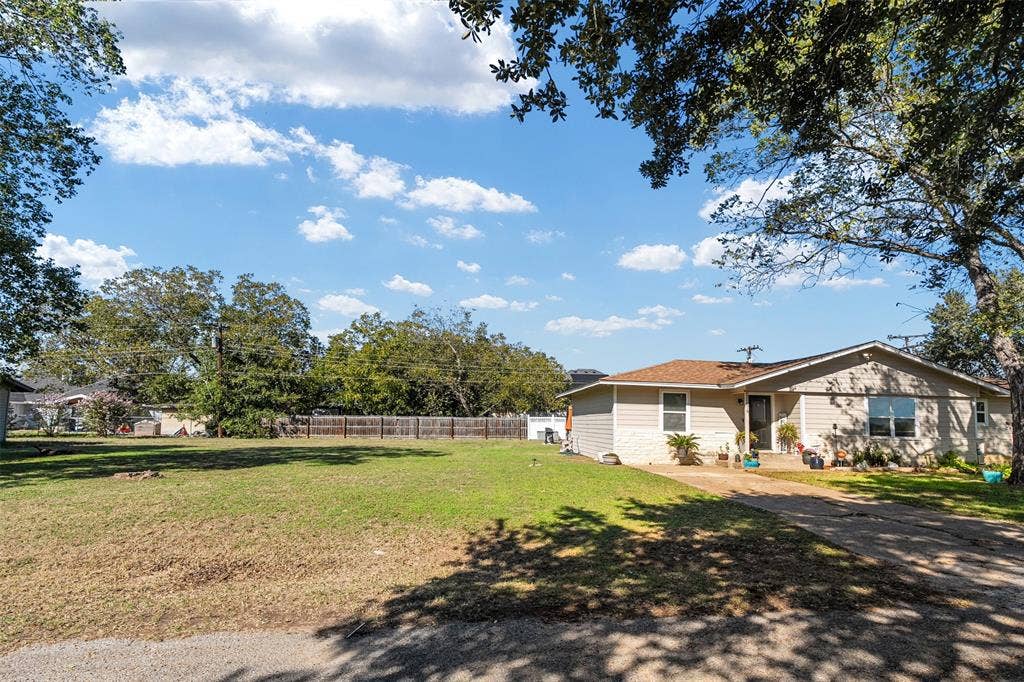 519 MAE Drive, Mabank, TX 75147 Exterior of a single-story residence featuring light-toned horizontal siding, a low-pitched roof, concrete driveway, and expansive front lawn with mature trees