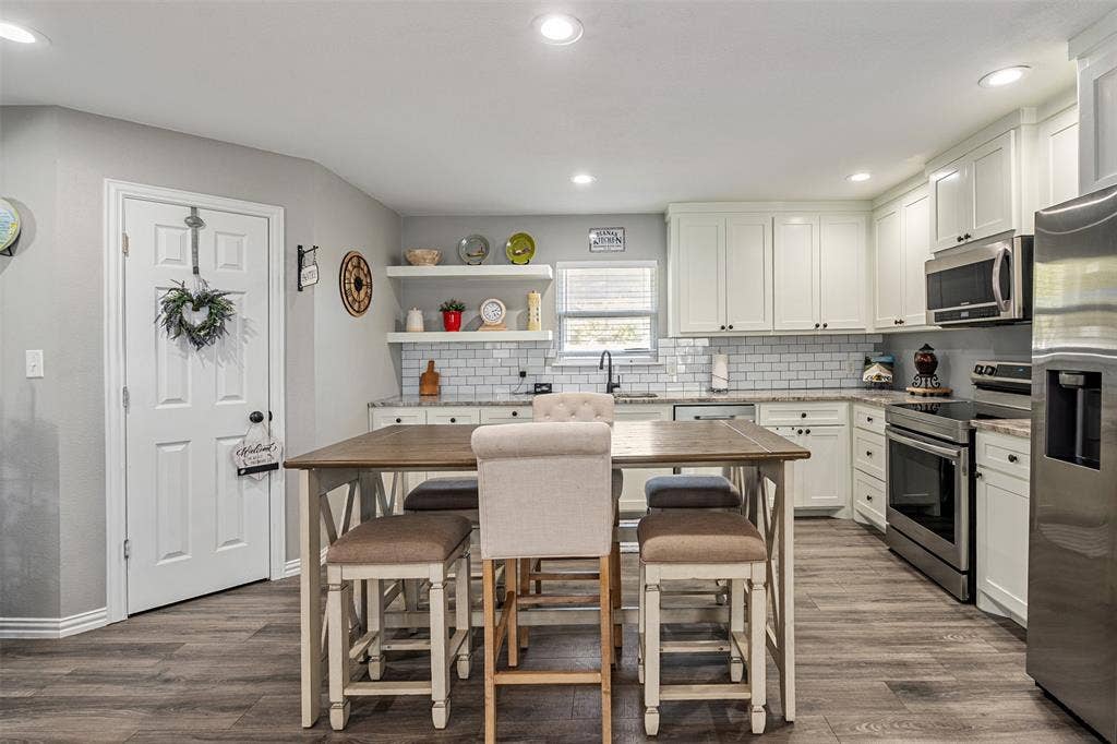 519 MAE Drive, Mabank, TX 75147 Kitchen featuring white shaker-style cabinetry, subway tile backsplash, stainless steel appliances, open floating shelving, and wood-finish flooring