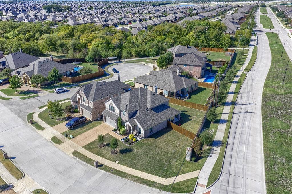 Aerial perspective of a multi-story residence featuring a brick and masonry exterior, hipped roofline, concrete driveway, and fenced rear yard