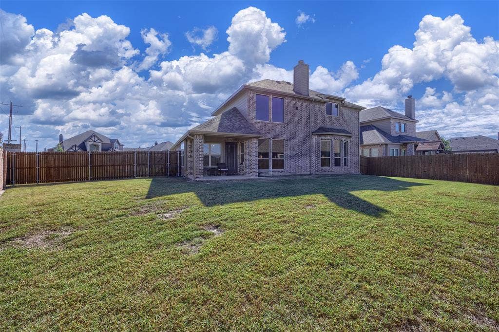 Brick exterior with a two-story elevation, expansive backyard, wooden privacy fencing, and covered patio area