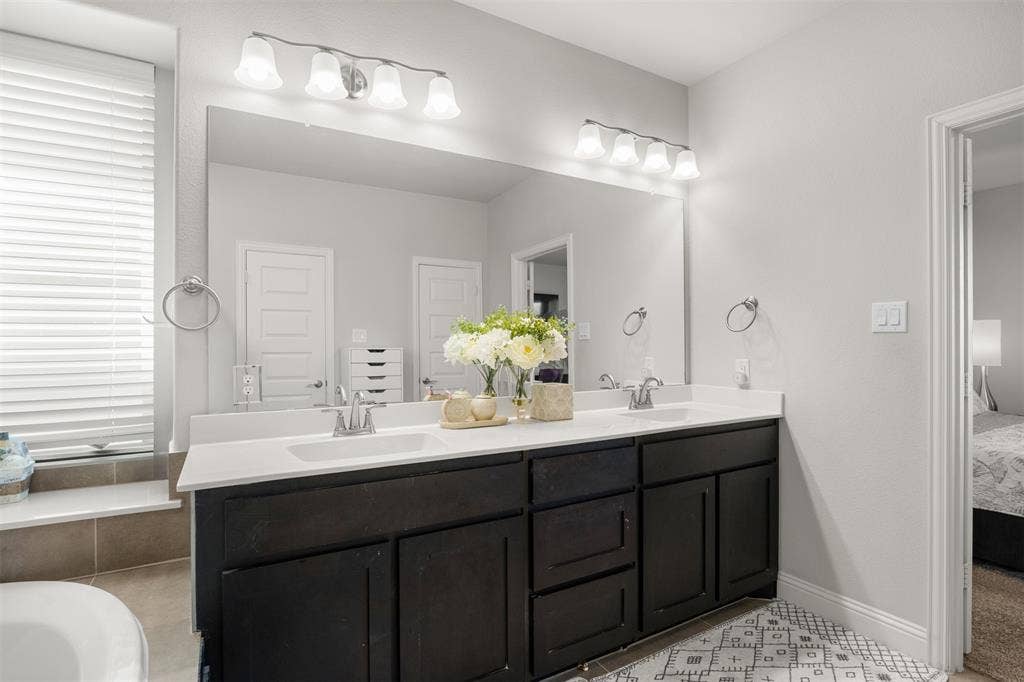 Double vanity featuring dark cabinetry, dual undermount sinks, solid surface countertops, two four-light fixtures, and a full-width wall mirror