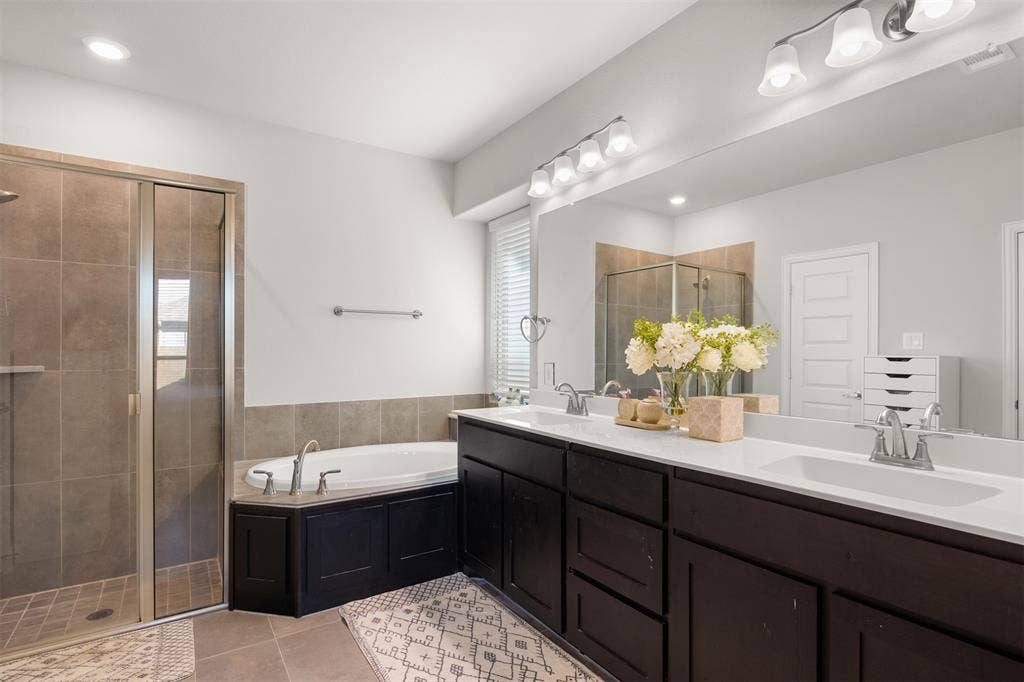 Double vanity with white countertops, integrated sinks, dark wood-finish cabinetry, separate soaking tub, and enclosed tile-surround shower