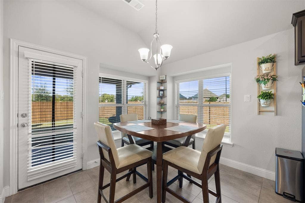 Dining area featuring vaulted ceilings, large windows with horizontal blinds, tiled flooring, and a central pendant light fixture