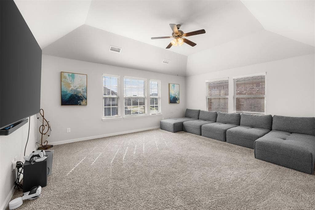 Vaulted ceiling, neutral wall-to-wall carpeting, multiple windows with blinds, and a ceiling fan with integrated lighting