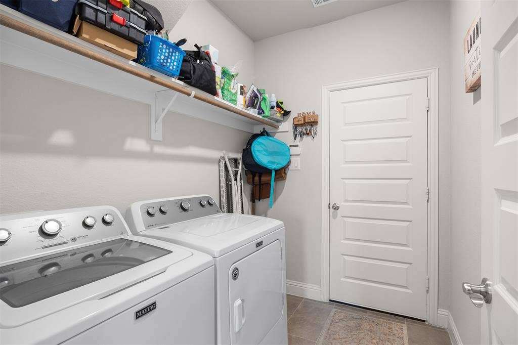 Laundry area featuring neutral-tone ceramic tile flooring, a multi-panel interior door with brushed metal hardware, and full-width wall-mounted shelving
