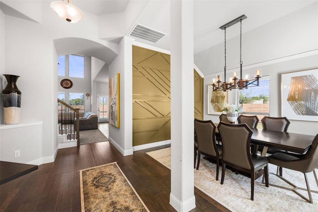 Interior featuring dark wood-finish flooring, soaring ceilings, geometric metallic wall detailing, and a multi-light industrial-style chandelier