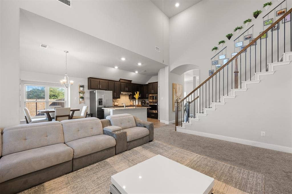 Vaulted ceilings, open-concept floor plan, kitchen featuring dark-stained cabinetry and a center island, and a staircase with metal balusters and a wood handrail