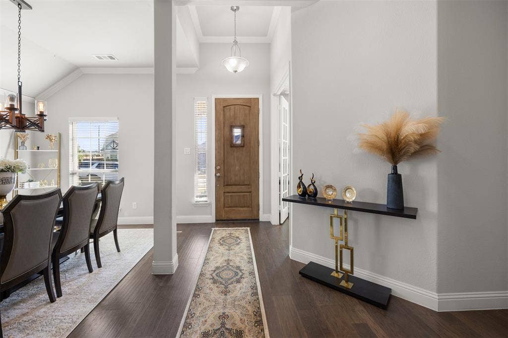 Foyer entry featuring dark wood-finish flooring, a solid wood front door with a decorative inset window, high ceilings with crown molding, and two pendant light fixtures