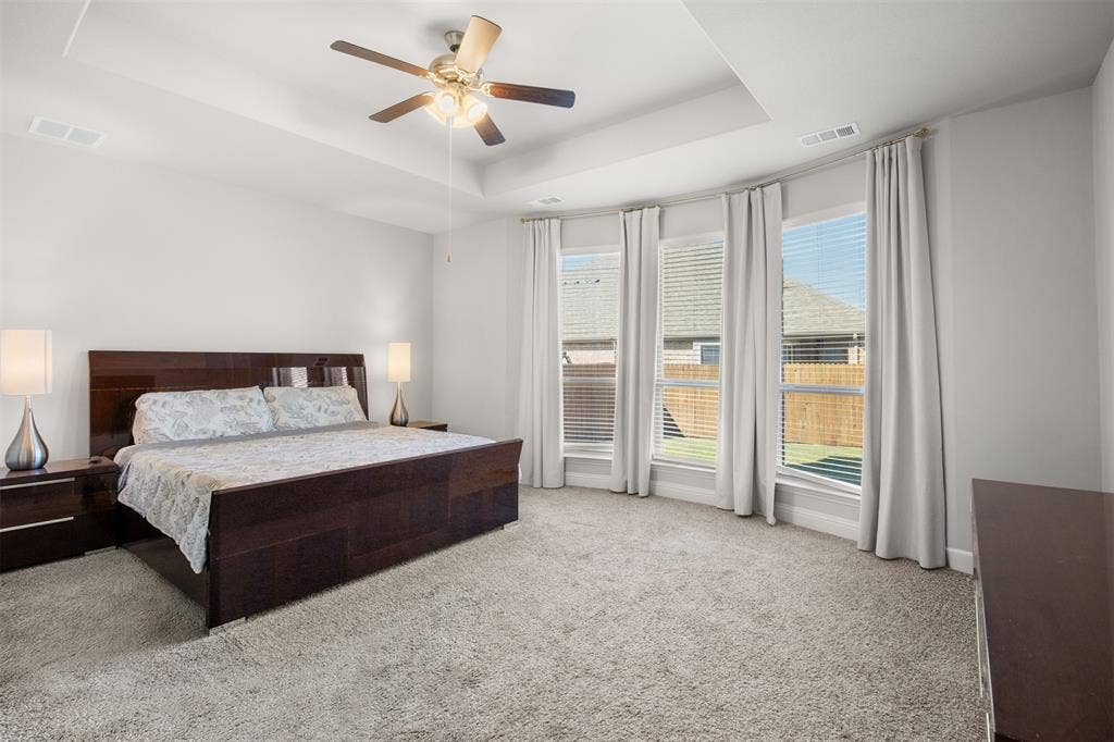Tray ceiling, neutral carpeting, and a triple-window configuration with natural lighting