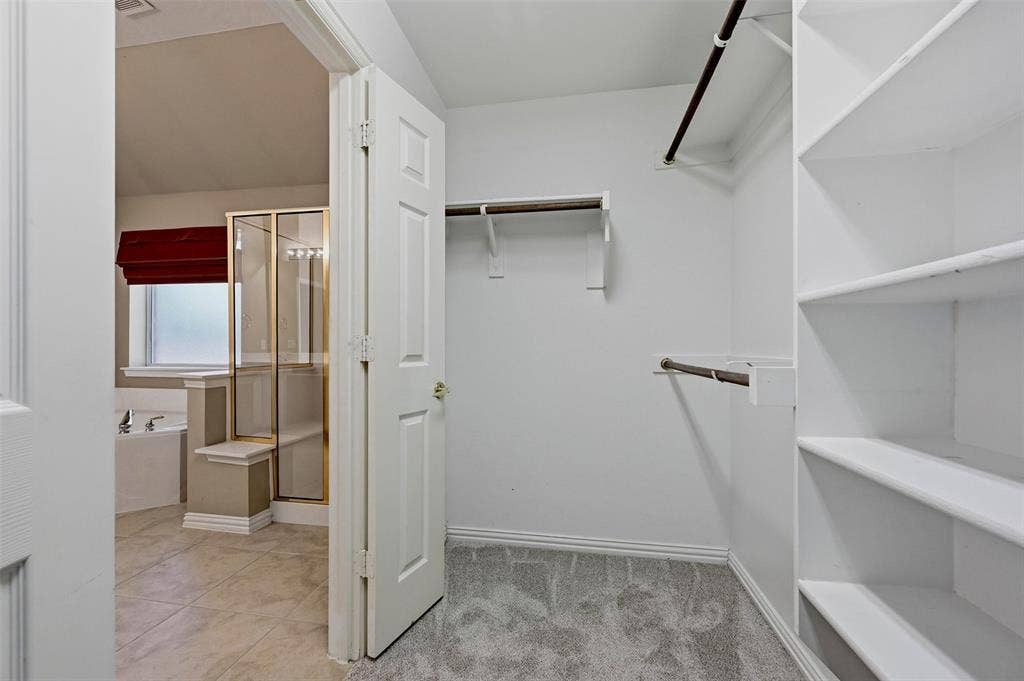 819 Mustang Drive, Fairview, TX 75069 Walk-in closet featuring white built-in shelving and dual hanging rods, with tiled flooring and a glass-enclosed shower visible beyond the doorway