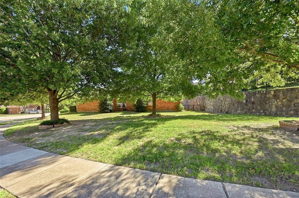819 Mustang Drive, Fairview, TX 75069 Expansive lawn featuring mature trees and a substantial stone retaining wall