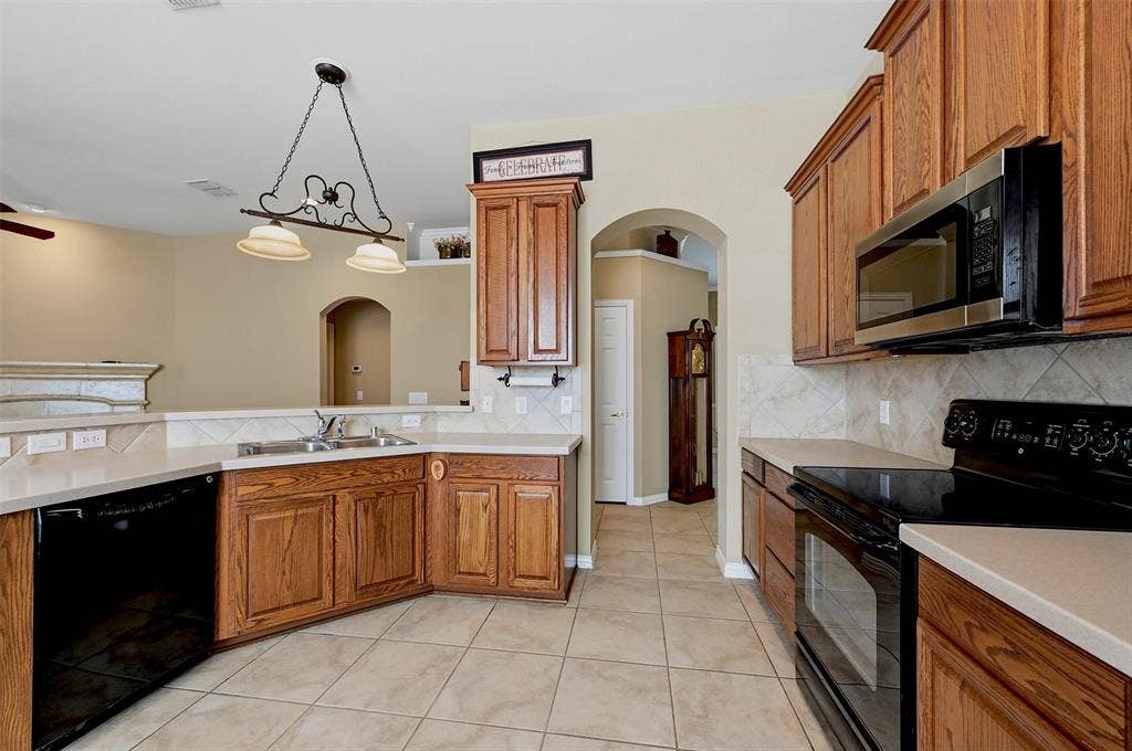 819 Mustang Drive, Fairview, TX 75069 Kitchen featuring wood cabinetry, solid-surface countertops, tile backsplash, tile flooring, and integrated black appliances