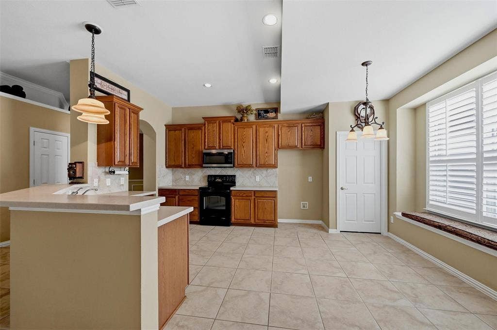 819 Mustang Drive, Fairview, TX 75069 Kitchen featuring stained wood cabinetry, stone-finish countertops, tile flooring, built-in black appliances, and a window seat with plantation shutters