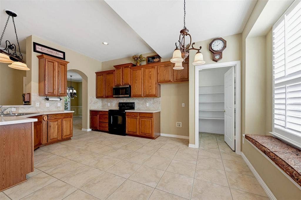 819 Mustang Drive, Fairview, TX 75069 Kitchen featuring wood cabinetry, tile flooring, built-in pantry with shelving, solid surface countertops, and a window seat with plantation shutters