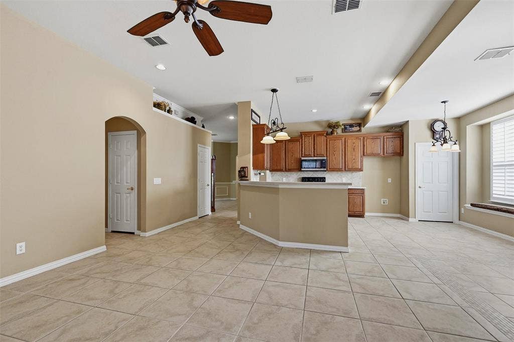 819 Mustang Drive, Fairview, TX 75069 Open-concept interior featuring large-format tile flooring, wood cabinetry, built-in breakfast bar, recessed lighting, and arched doorway entry