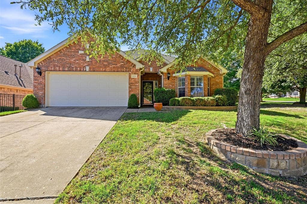 819 Mustang Drive, Fairview, TX 75069 Brick exterior featuring a gabled roofline, front-facing two-car garage, bay window, and a raised brick tree well