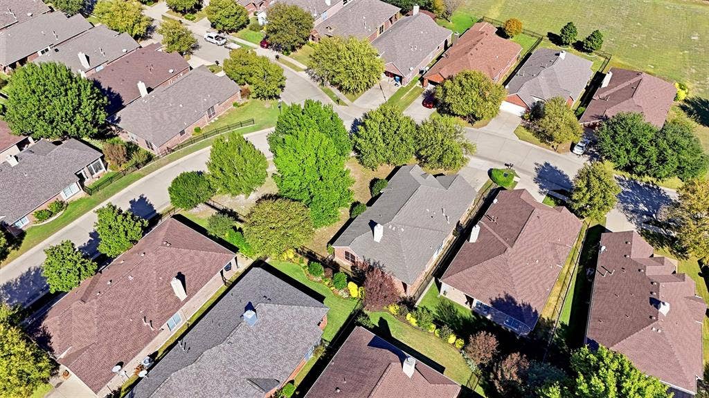 819 Mustang Drive, Fairview, TX 75069 Aerial perspective of a brick residence situated on a corner lot, featuring a multi-gabled roofline, a prominent chimney, a side-entry garage, and mature landscaping