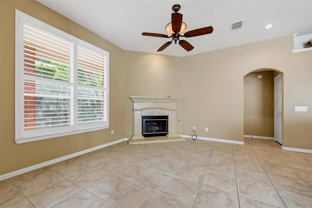 819 Mustang Drive, Fairview, TX 75069 Ceramic tile flooring, stone-surround fireplace, multi-pane window with plantation shutters, ceiling fan with integrated light fixture, and arched entryway