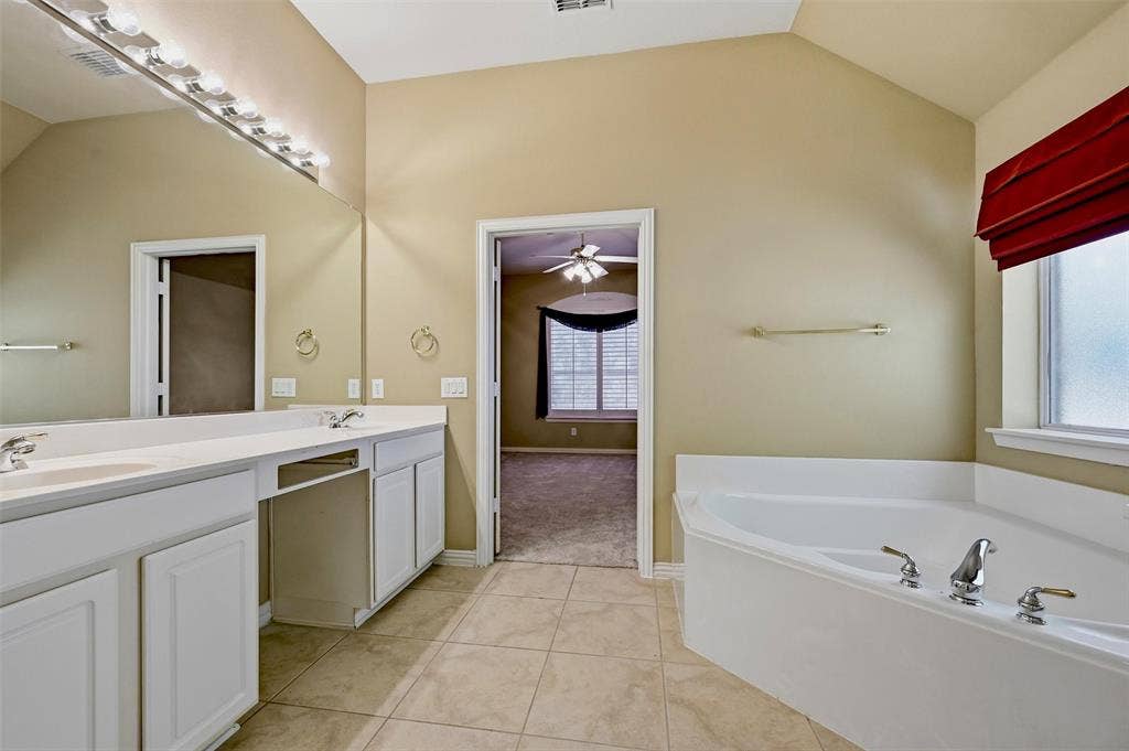819 Mustang Drive, Fairview, TX 75069 Bathroom featuring a dual-sink vanity with white cabinetry, a large wall-to-wall mirror, ceramic tile flooring, and a corner soaking tub