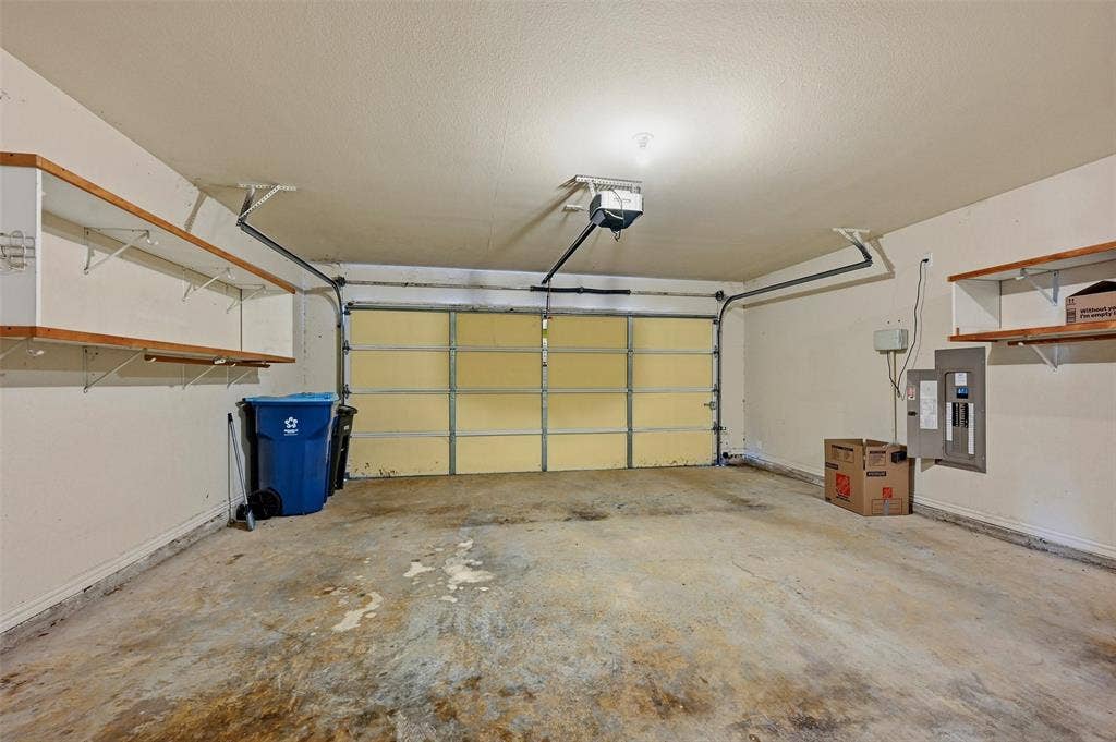 819 Mustang Drive, Fairview, TX 75069 Multi-car garage featuring a concrete floor, built-in wooden shelving, and an integrated overhead door opener
