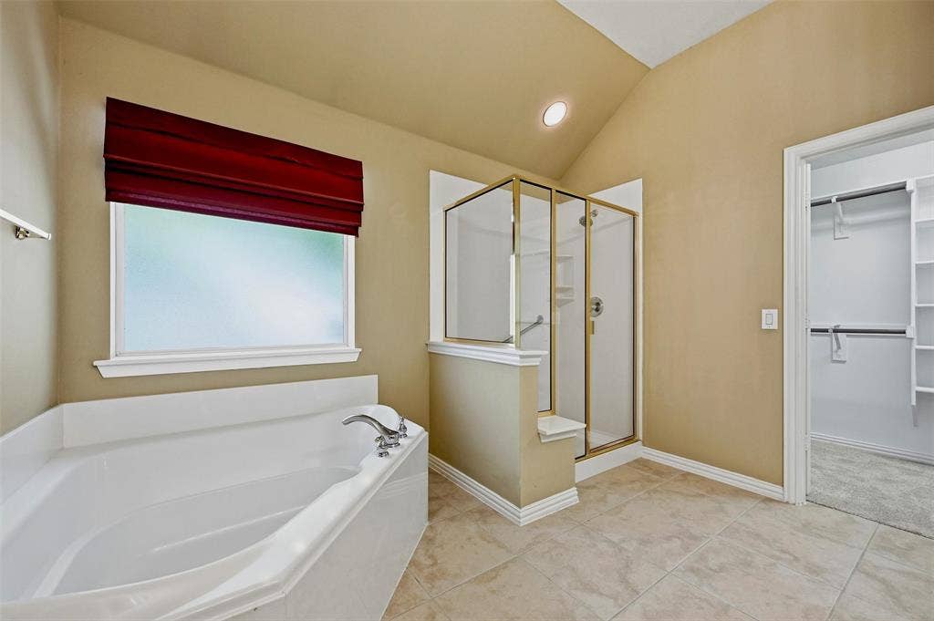 819 Mustang Drive, Fairview, TX 75069 Bathroom featuring a white soaking tub, a separate glass-enclosed shower with gold-tone framing, tile flooring, and a walk-in closet with built-in shelving