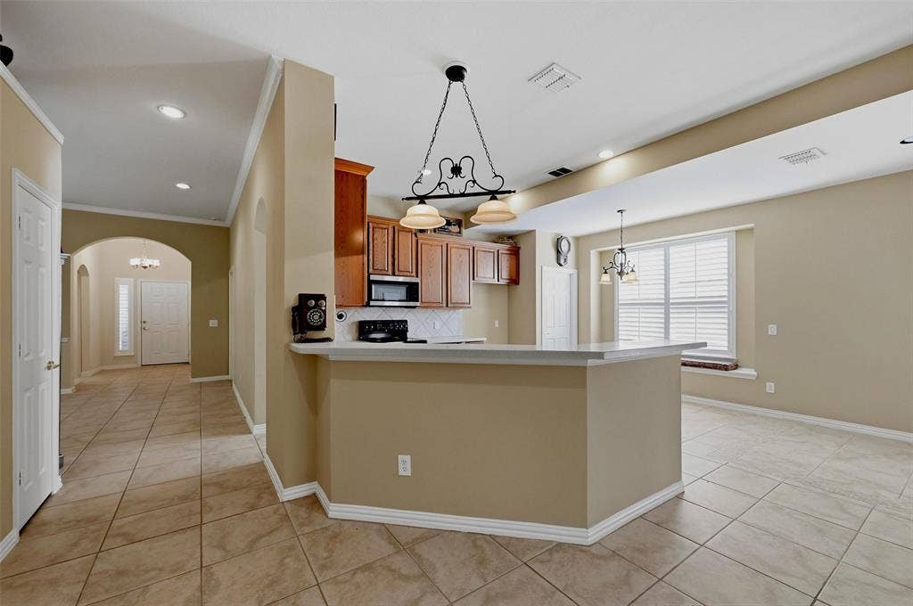 819 Mustang Drive, Fairview, TX 75069 Kitchen featuring raised-panel wood cabinetry, a breakfast bar with stone-finish countertop, tile flooring, recessed lighting, and a decorative wrought iron pendant fixture