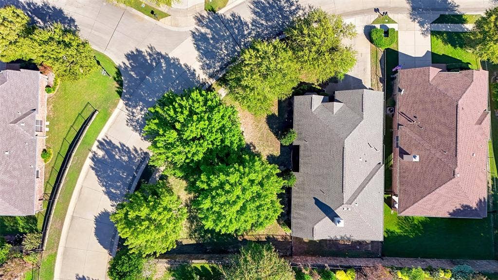 819 Mustang Drive, Fairview, TX 75069 Aerial perspective of a corner lot featuring mature trees, a multi-pitched roofline, an exterior chimney, and a private rear yard with perimeter fencing