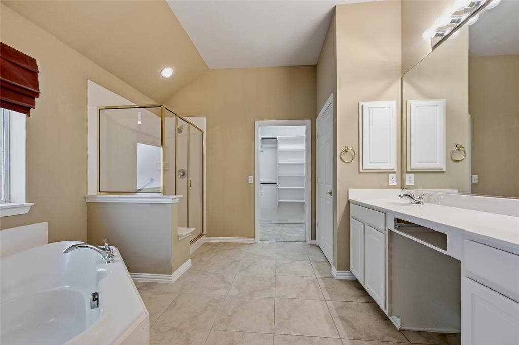 819 Mustang Drive, Fairview, TX 75069 Bathroom featuring a soaking tub, glass-enclosed shower with gold-tone hardware, white dual-sink vanity with light-toned countertop, and built-in closet shelving