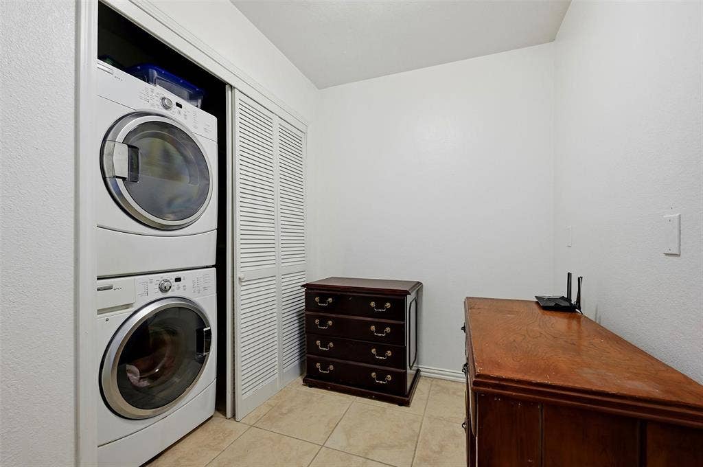 819 Mustang Drive, Fairview, TX 75069 Laundry area featuring stacked front-load washer and dryer, white louvered bifold closet doors, and neutral square tile flooring
