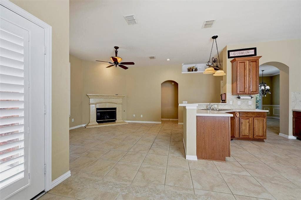 819 Mustang Drive, Fairview, TX 75069 Open-concept interior featuring tile flooring, a fireplace with a decorative mantel, wood cabinetry, stone-style countertops, and arched entryways