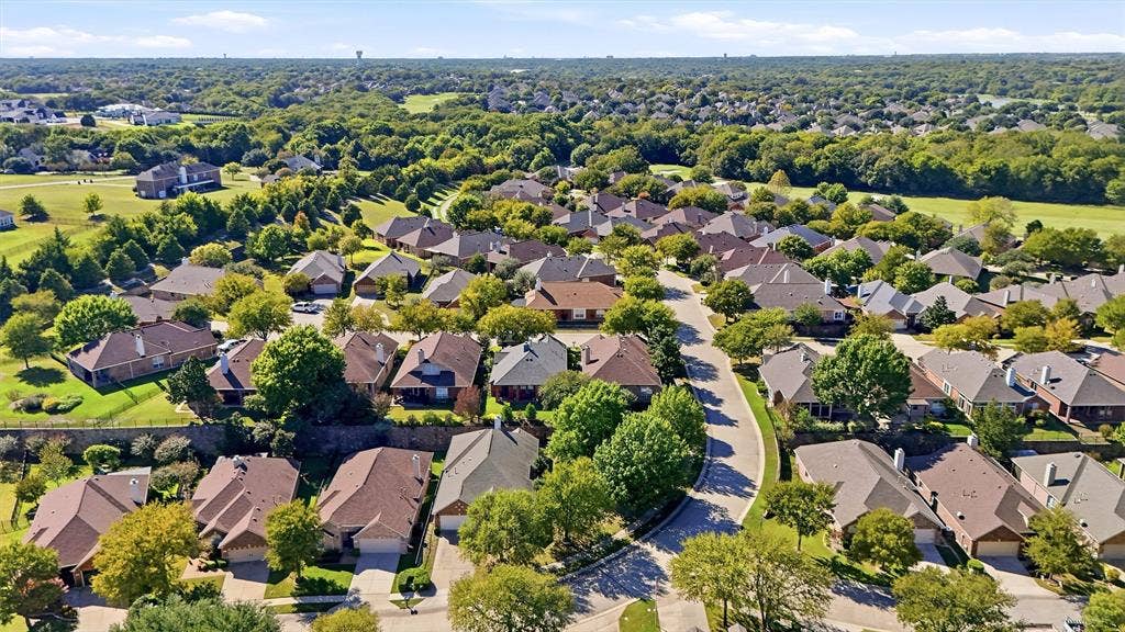 819 Mustang Drive, Fairview, TX 75069 Aerial perspective of a residential neighborhood featuring paved streets, mature trees, dense greenery, and detached homes with shingled rooflines