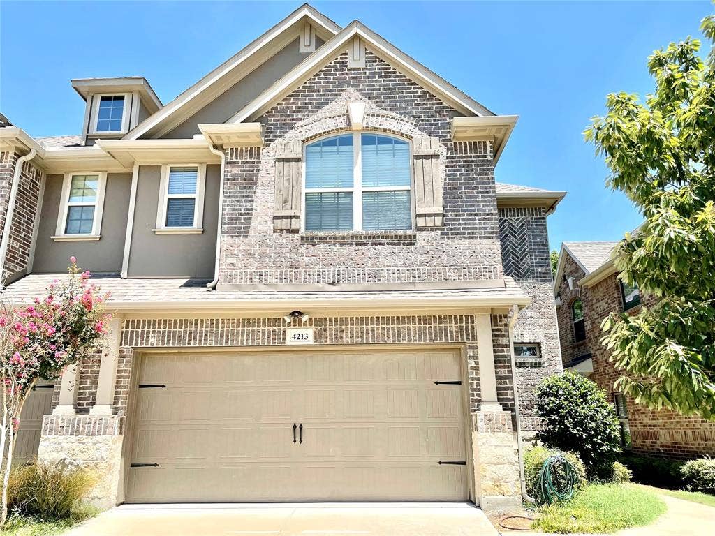 4213 Arbrook Way, Plano, TX 75074 Multi-level brick and stone façade featuring decorative shutters, a gabled roofline, an arched window, and an attached two-car garage