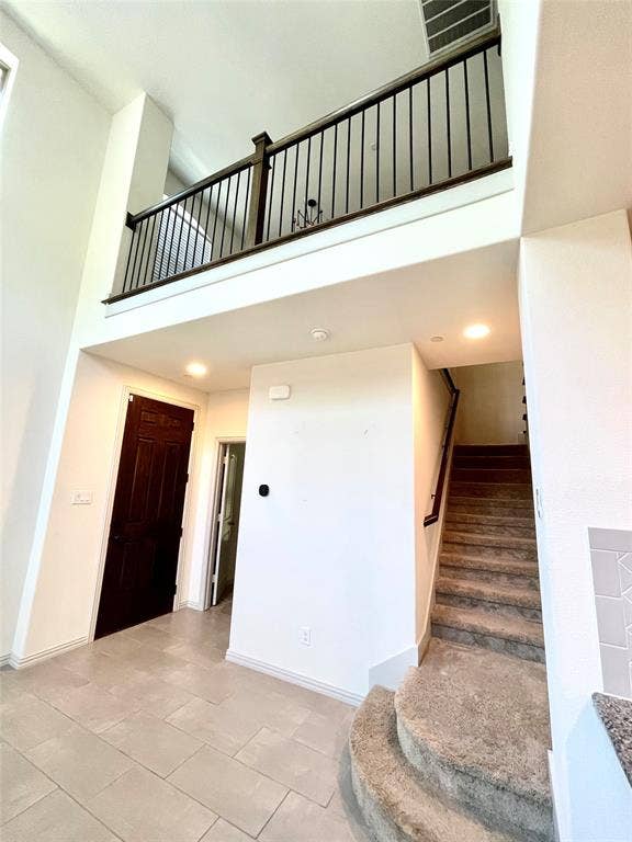 4213 Arbrook Way, Plano, TX 75074 High-ceiling entryway featuring ceramic tile flooring, a staircase with carpeted treads, and a landing with a dark-finished metal balustrade