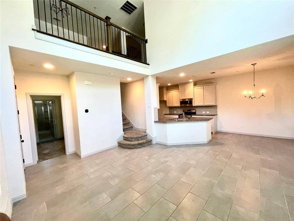 4213 Arbrook Way, Plano, TX 75074 Open-concept interior featuring double-height ceilings, a multi-level staircase with carpeted treads, a kitchen island with stone-finish countertops, light-toned cabinetry, and tile flooring