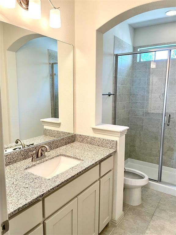 4213 Arbrook Way, Plano, TX 75074 Bathroom featuring a stone-composite countertop with an integrated basin, shaker-style cabinetry, framed wall mirror, arched architectural detailing, and a walk-in shower with tile surround