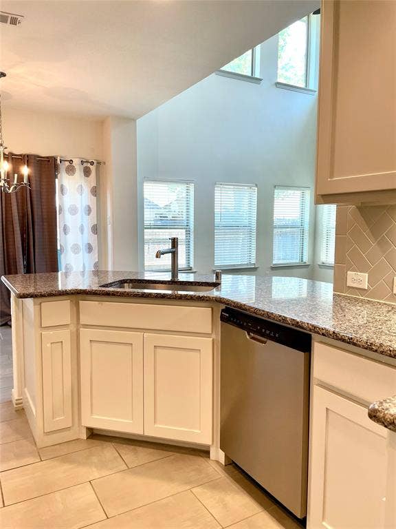 4213 Arbrook Way, Plano, TX 75074 Kitchen featuring a stone countertop, stainless steel dishwasher, shaker-style cabinetry, herringbone-patterned tile backsplash, and double-height ceiling with clerestory windows