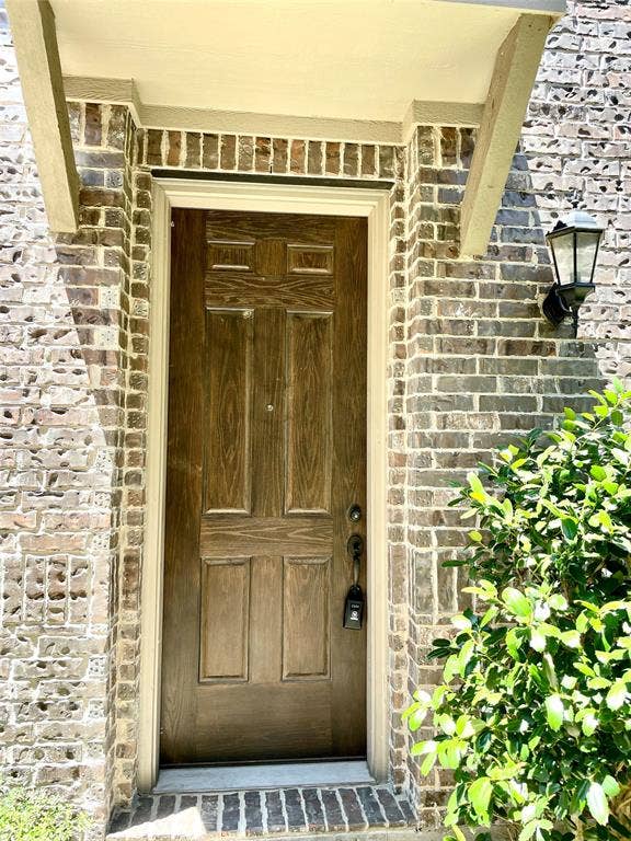 4213 Arbrook Way, Plano, TX 75074 Entryway featuring a wood-finish door, brick exterior facade, metal lantern-style light fixture, and arched covered threshold