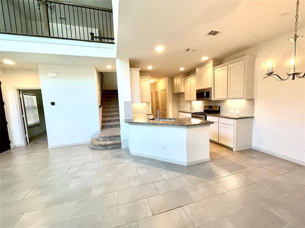 4213 Arbrook Way, Plano, TX 75074 Kitchen featuring light-toned cabinetry, stone-finish countertops, and stainless steel built-in appliances, complemented by tile flooring, a two-story ceiling, and a metal balustrade