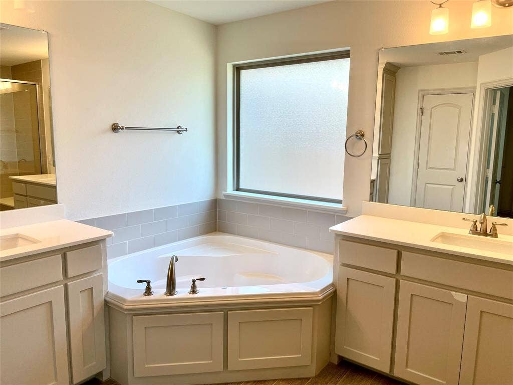 4213 Arbrook Way, Plano, TX 75074 Corner soaking tub with tile surround, dual vanities featuring light-tone cabinetry, surface-mounted mirrors, and chrome fixtures