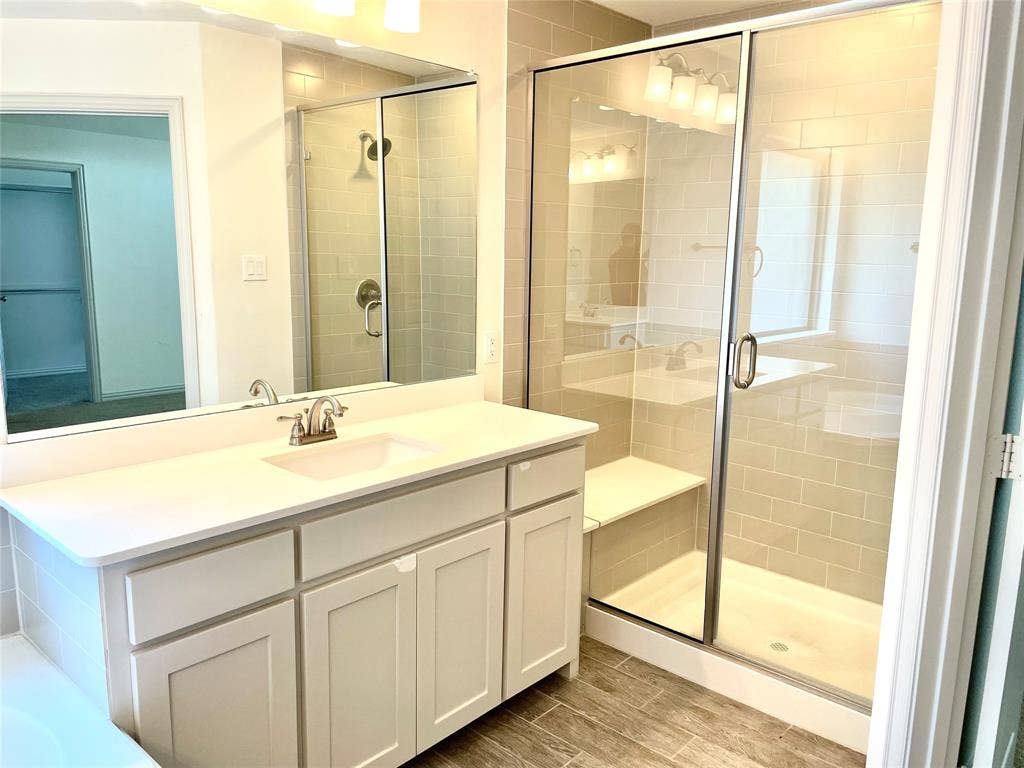 4213 Arbrook Way, Plano, TX 75074 Bathroom featuring a white cabinetry vanity with a solid surface countertop, rectangular under-mount sink, walk-in shower with a glass enclosure and built-in bench, subway tile shower surround, and wood-finish flooring