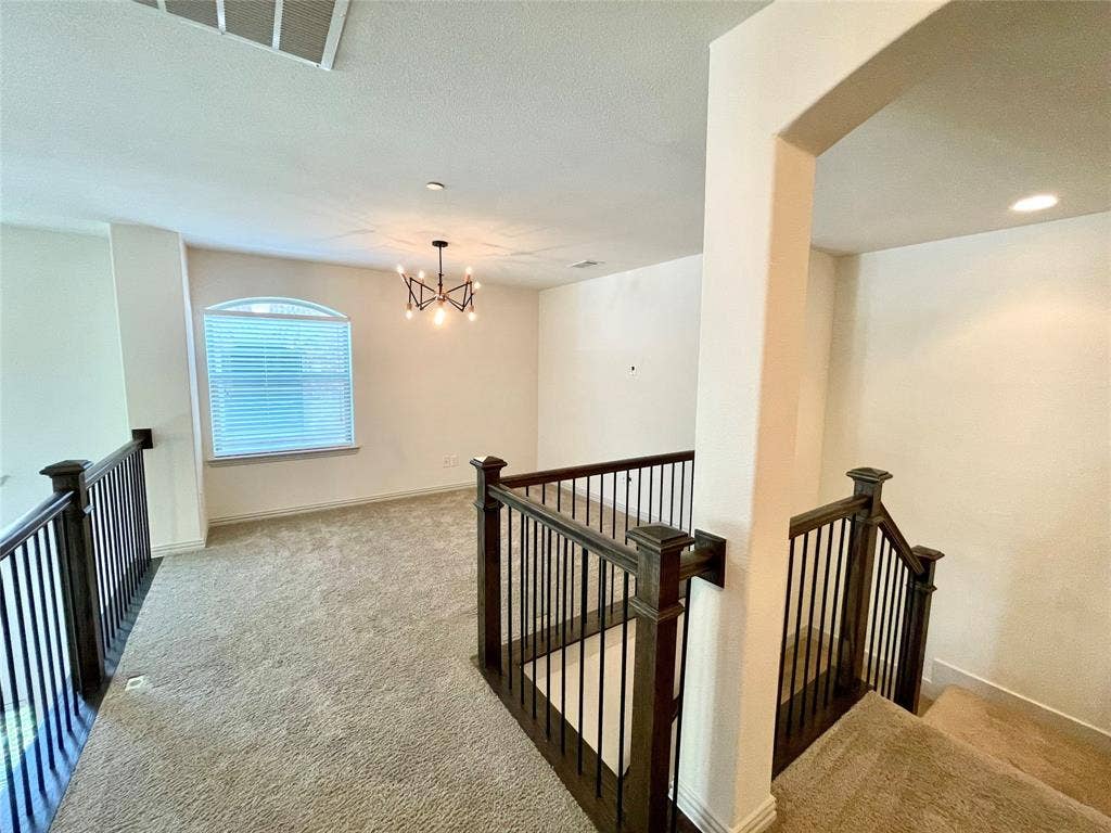 4213 Arbrook Way, Plano, TX 75074 Open interior space featuring arched window, wall-to-wall carpeting, multi-arm chandelier, and staircase with wooden handrails and metal balusters